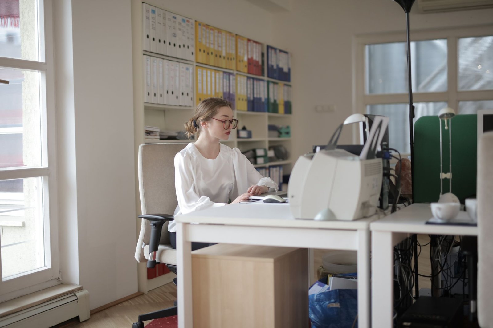 Accountant working at a desk beside shelves of colour-coded files in a bright office